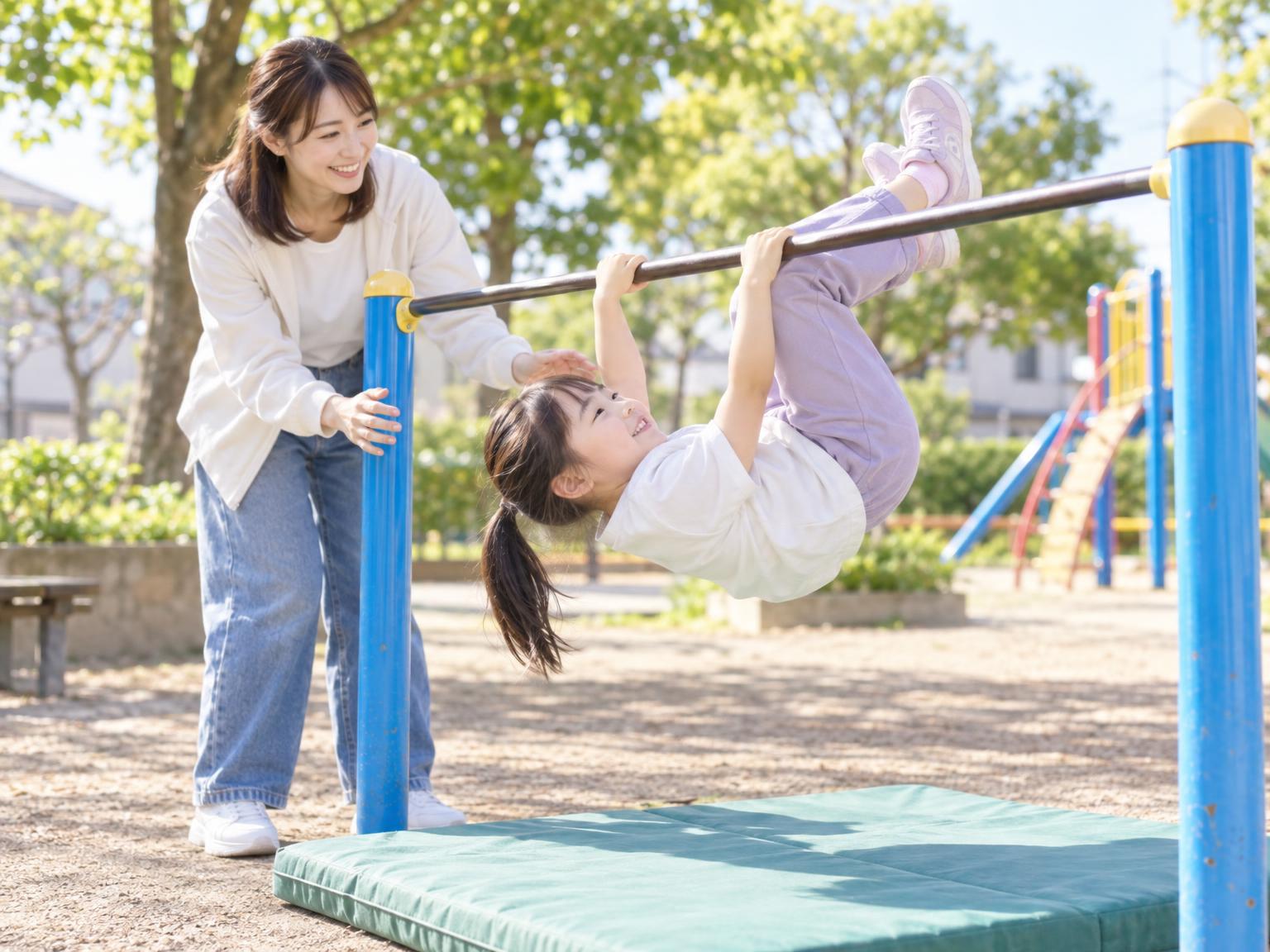 鉄棒で逆上がりを練習する小学生と見守る保護者