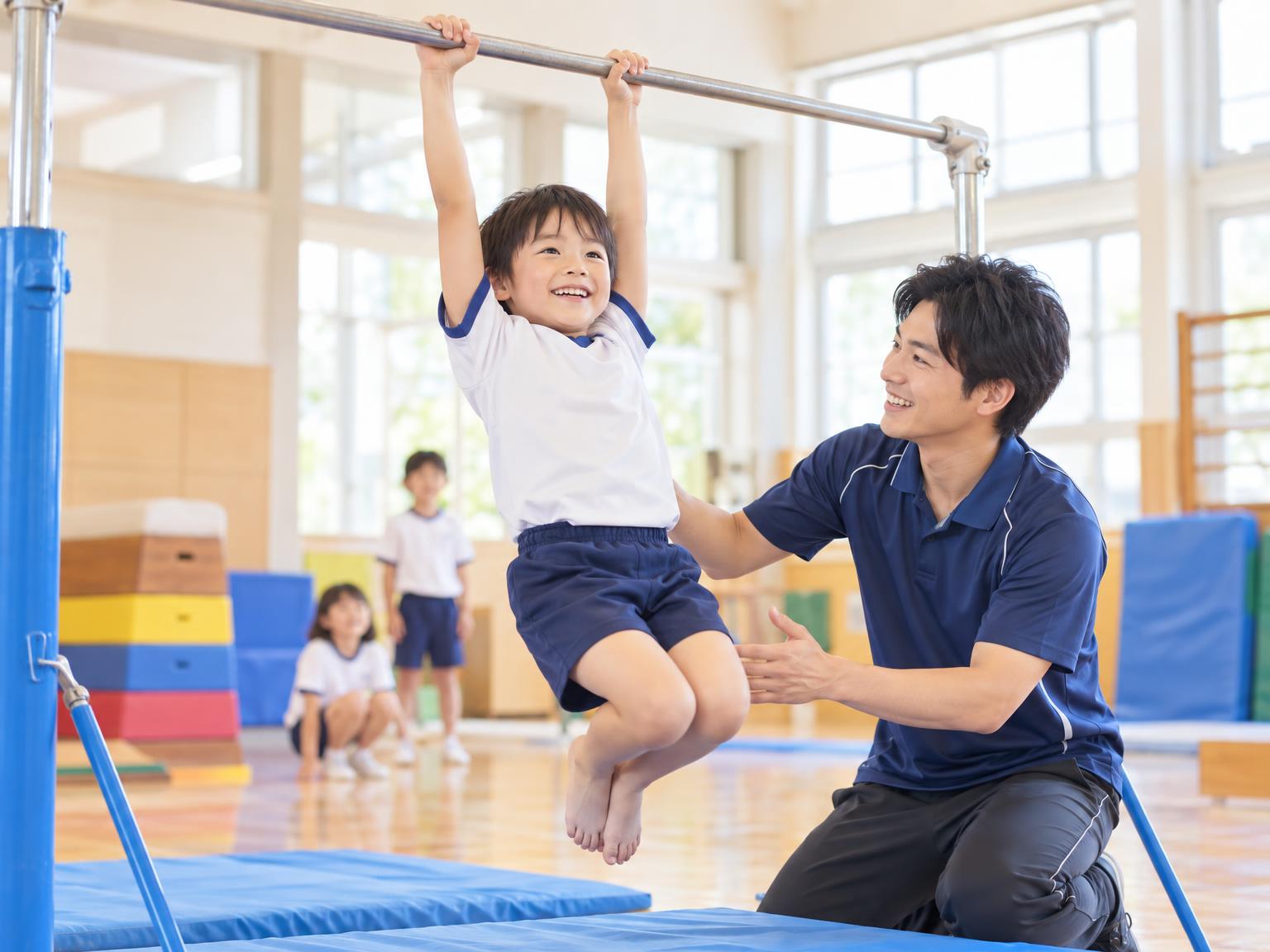 体操教室で鉄棒の練習をする小学生とコーチ