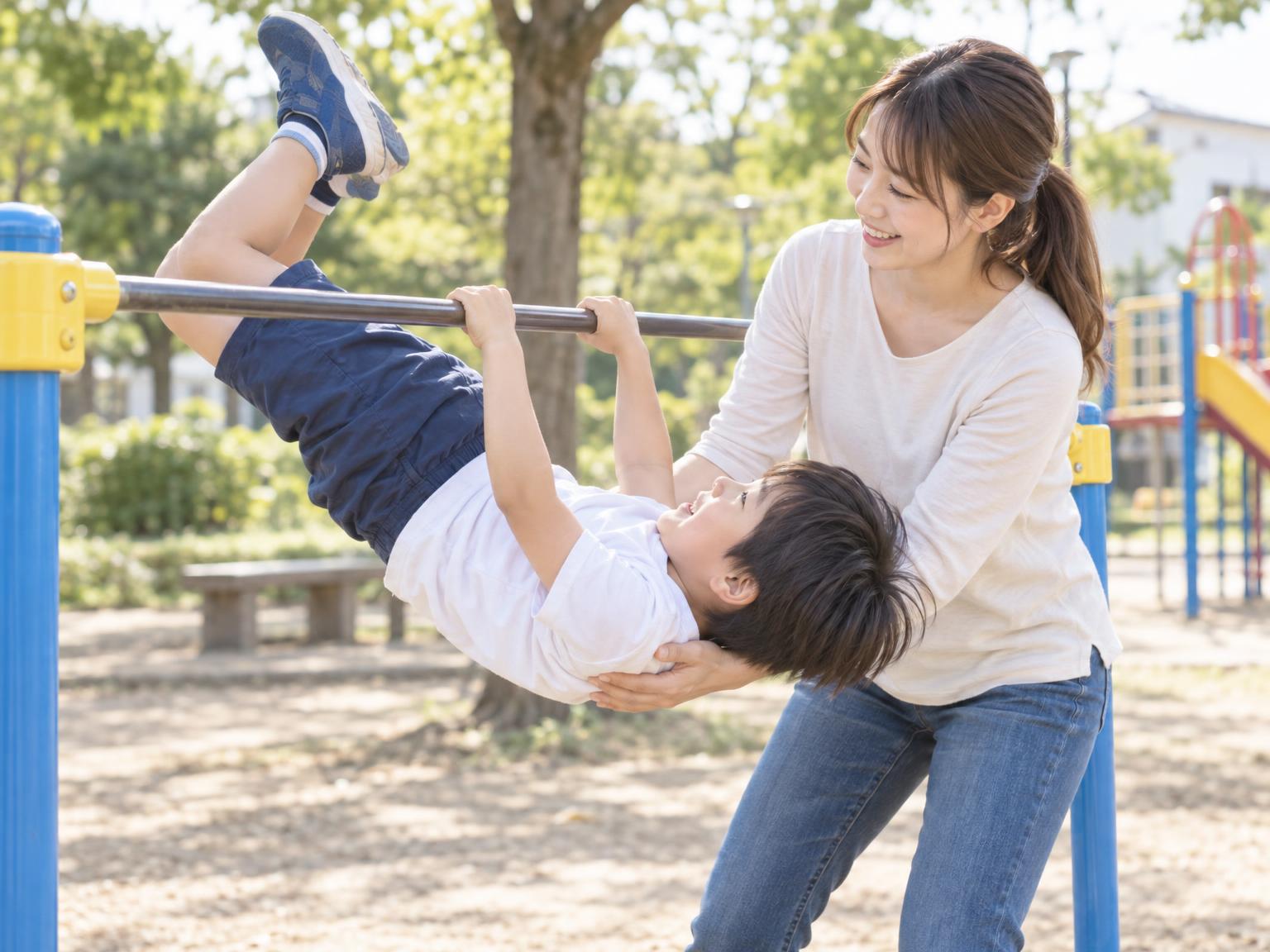 保護者が補助しながら鉄棒で逆上がりを練習する小学生