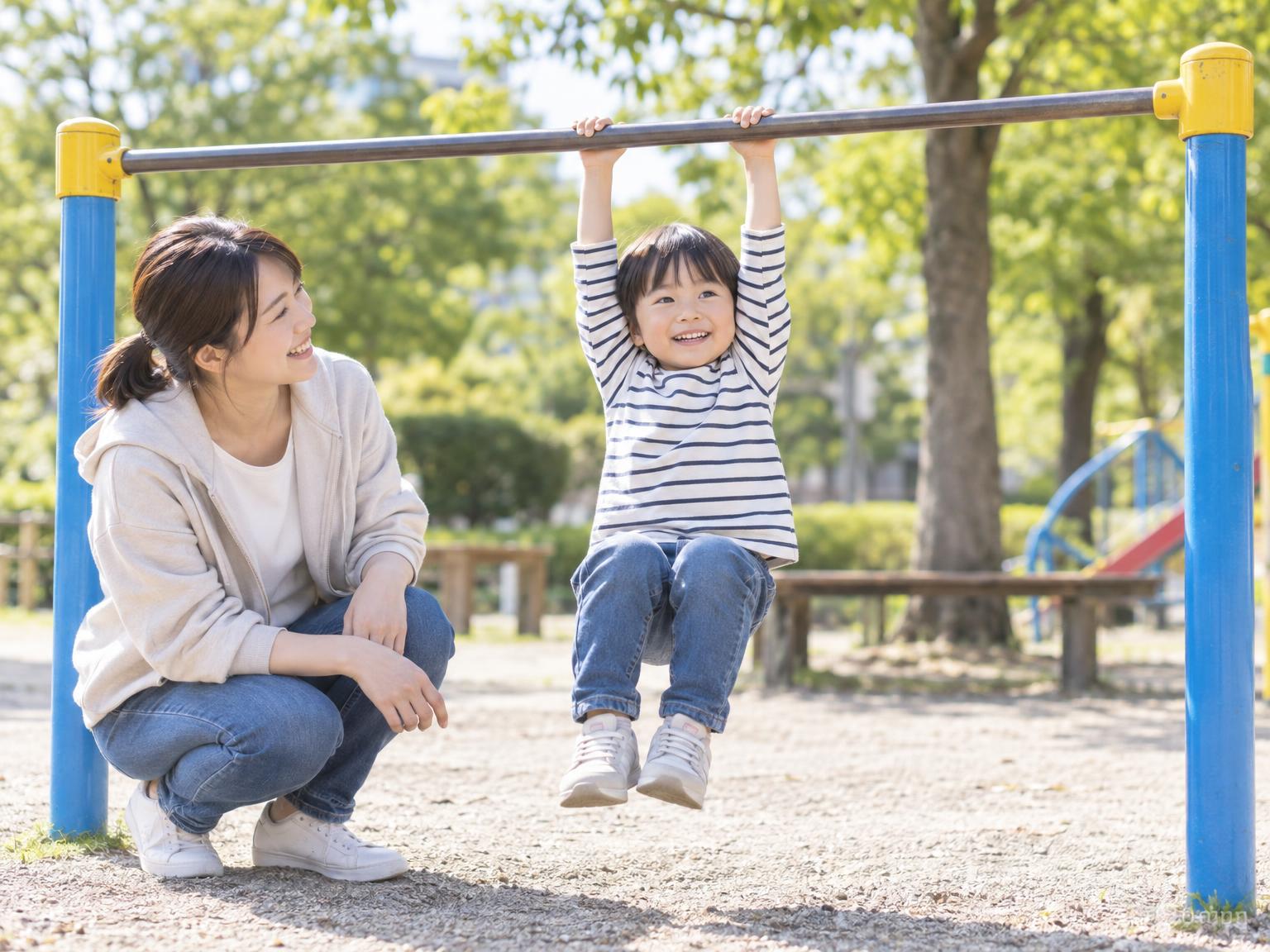 公園の鉄棒にぶら下がる幼児と見守る保護者