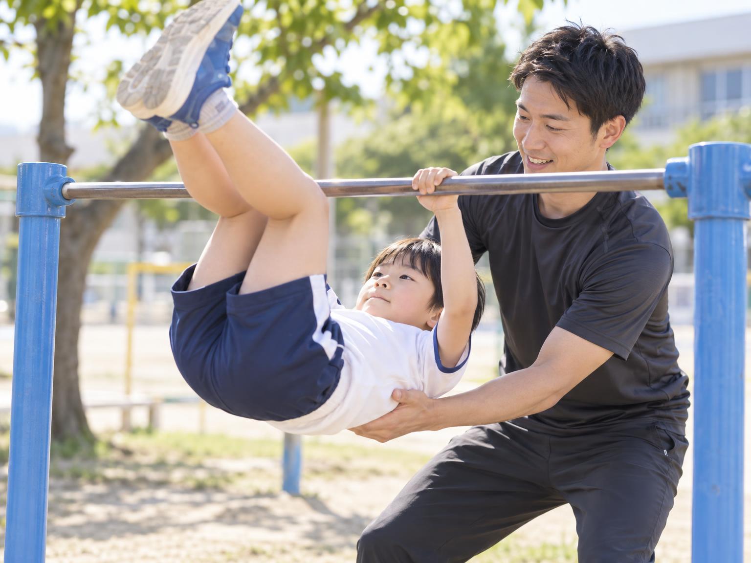指導者のサポートを受けながら鉄棒で逆上がりを練習する小学生