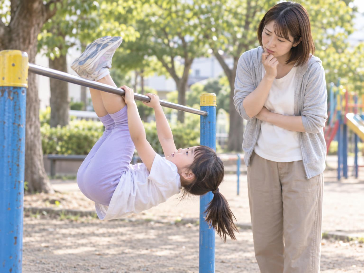 保護者が見守る中、鉄棒で逆上がりの練習をする子ども