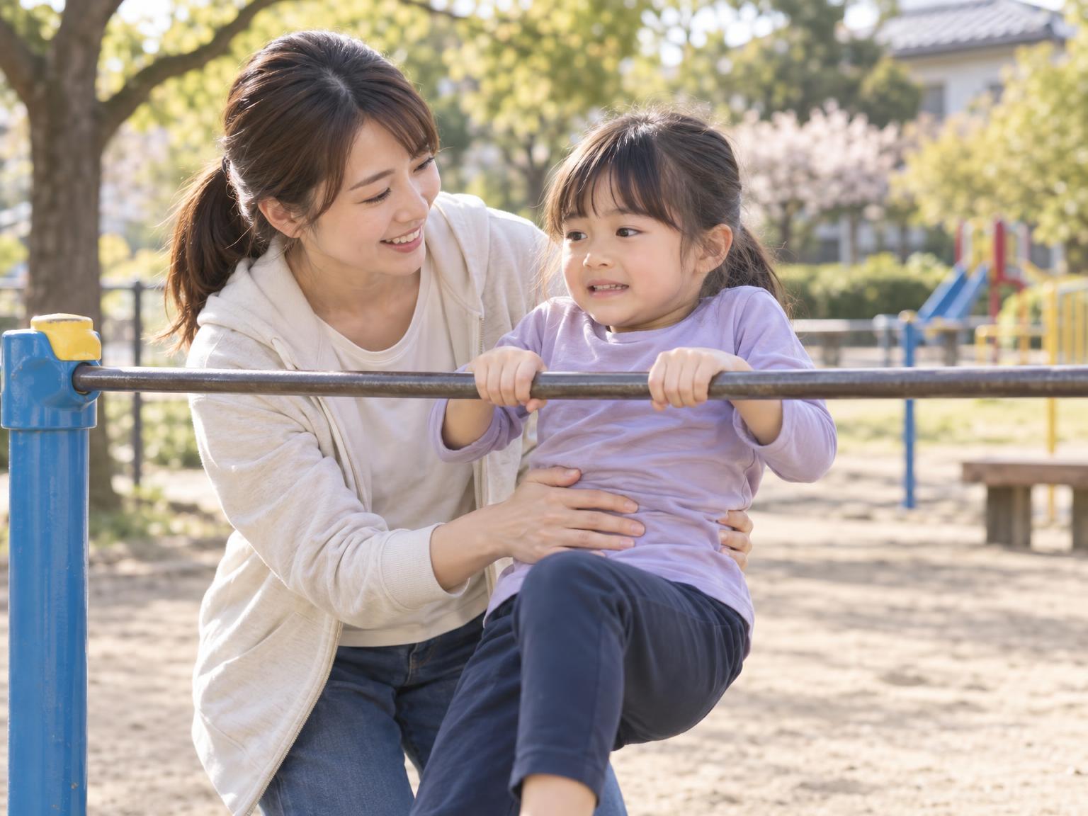 保護者が子どもの腰と背中を支えながら鉄棒の練習を補助している様子