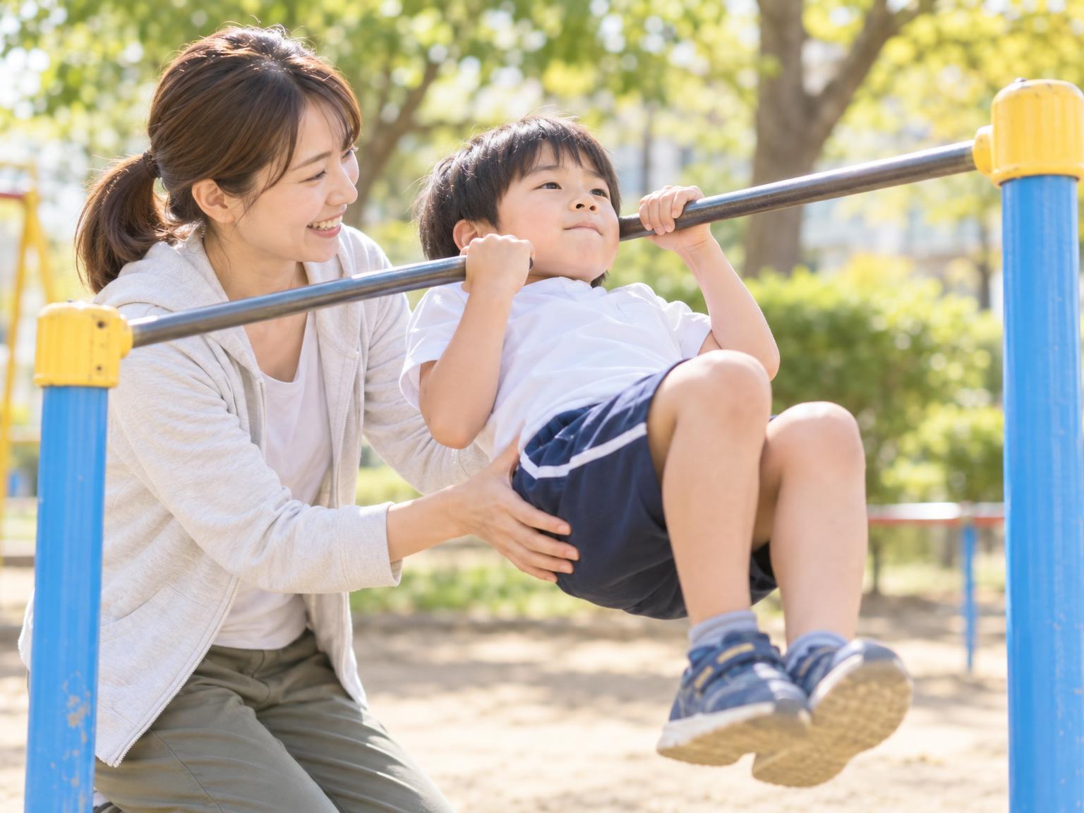 保護者が補助しながら逆上がりの練習をする小学生