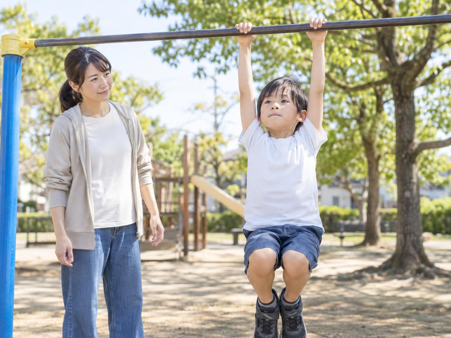 鉄棒にぶら下がる小学生と見守る保護者