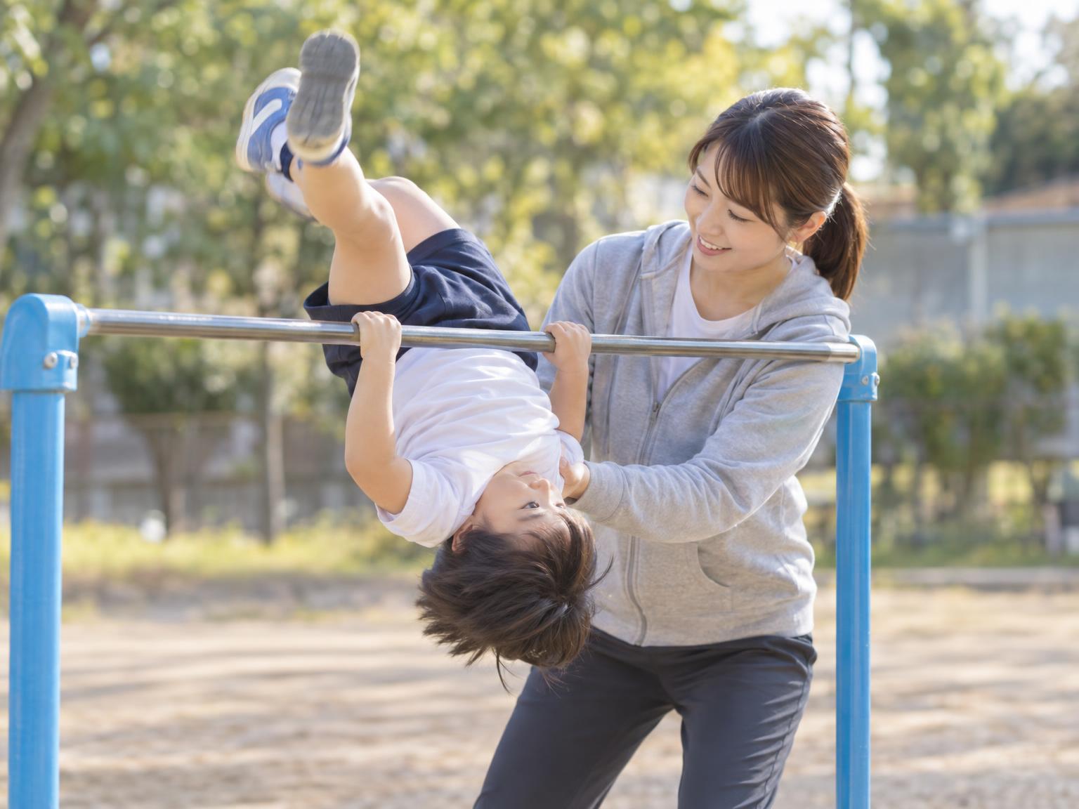 補助具とコーチのサポートを受けながら鉄棒の逆上がりに取り組む子ども