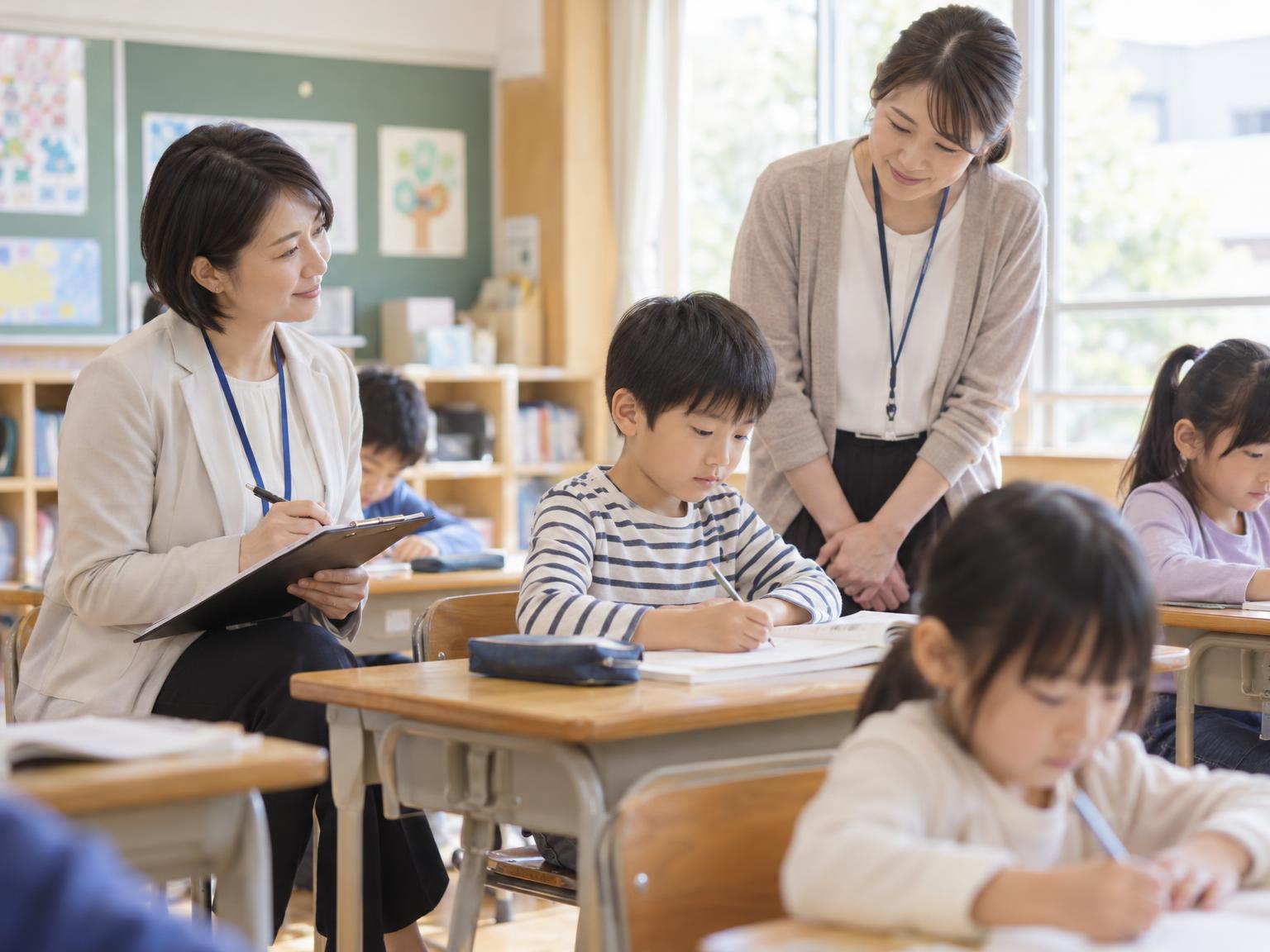 訪問員が学校の教室で子どもの様子を観察し、担任と情報を共有している場面のイラスト