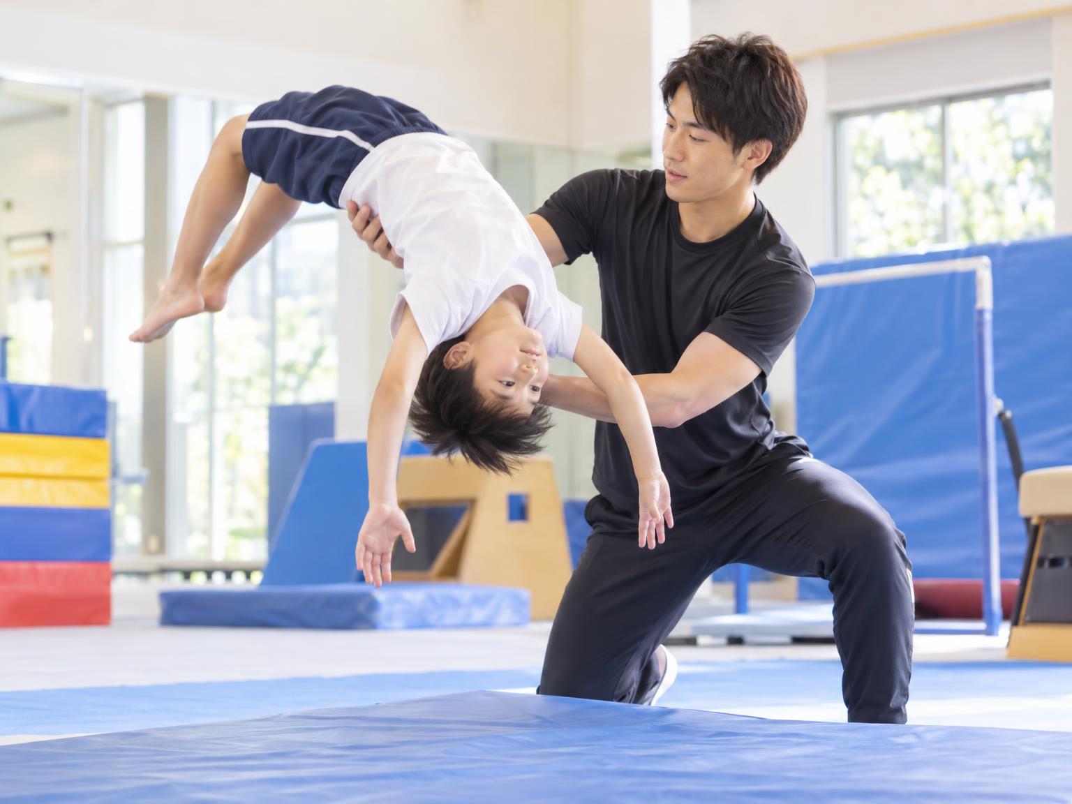 コーチが補助しながら子どもがバク転を練習している室内の体操スタジオ