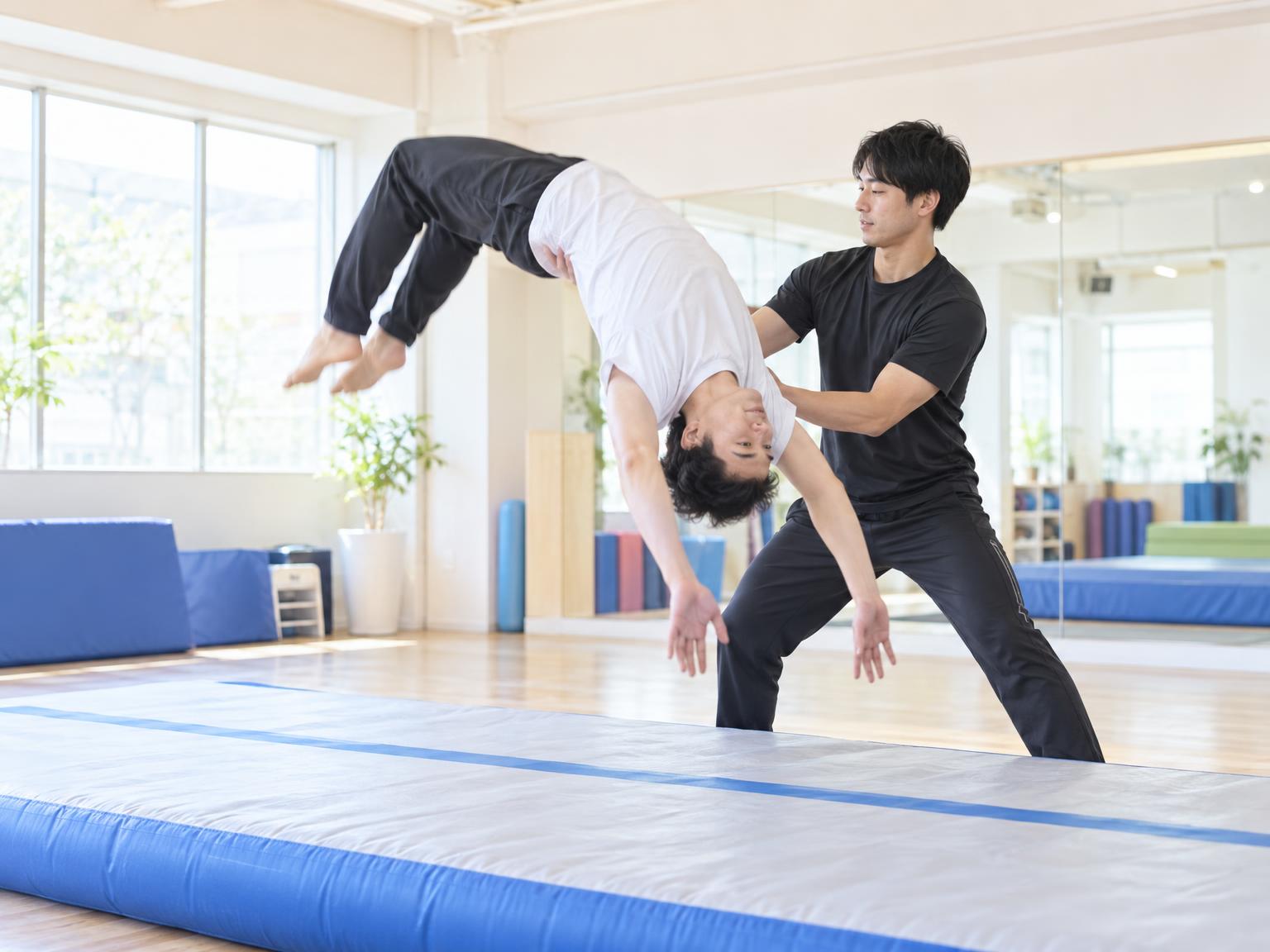 インストラクターの補助を受けながらバク転を練習する大人の男性